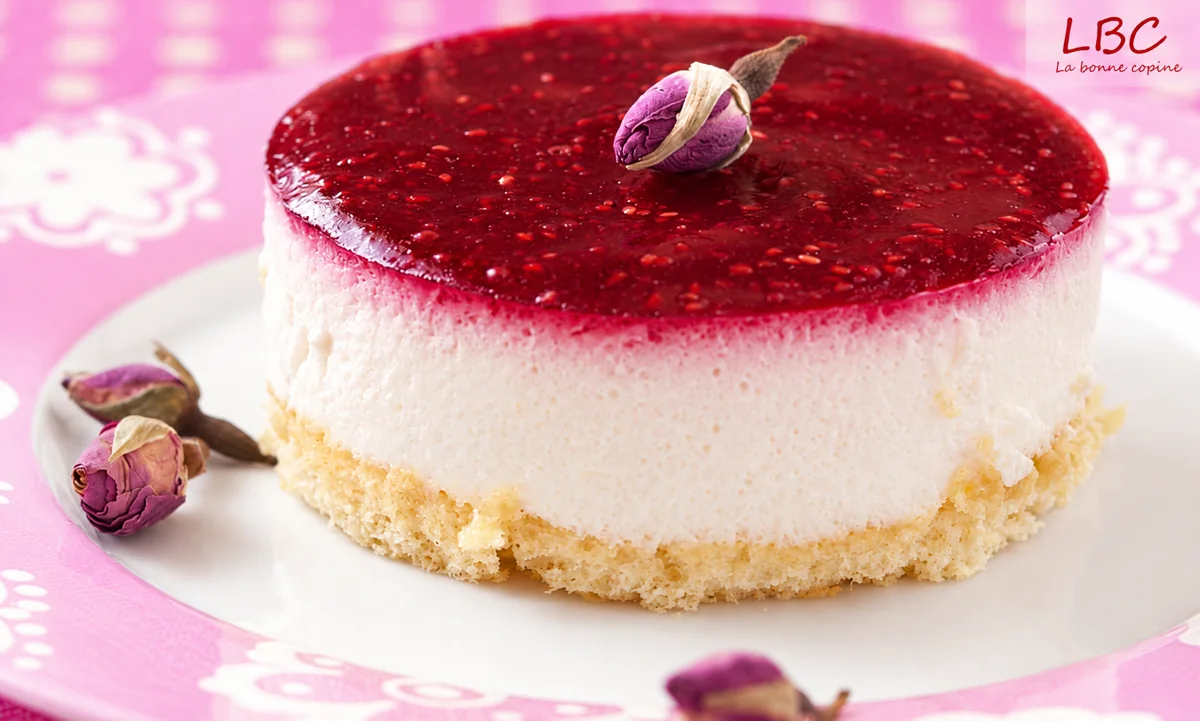 Entremets rond à la mousse blanche et au nappage rouge, décoré de boutons de rose séchés.