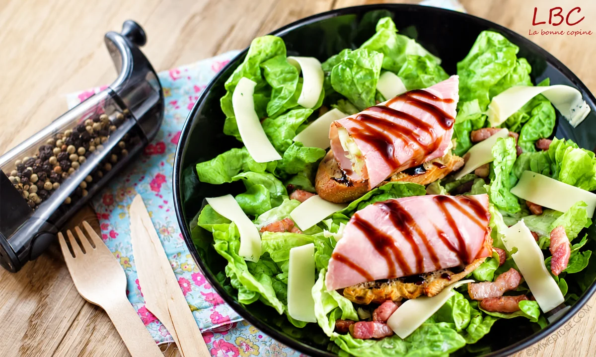Deux tartines au jambon et à la sauce brune sur une salade verte, avec copeaux de fromage et lardons.