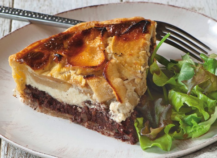 Une part de tarte aux poires et au boudin noir, avec sa cro&ucirc;te dor&eacute;e, servie sur une assiette blanche accompagn&eacute;e de salade verte et d&rsquo;une fourchette