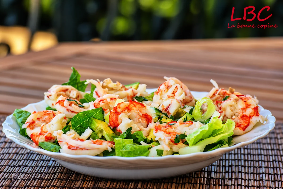 Salade de crevettes et feuilles vertes dans une assiette blanche sur un set de table tissé.