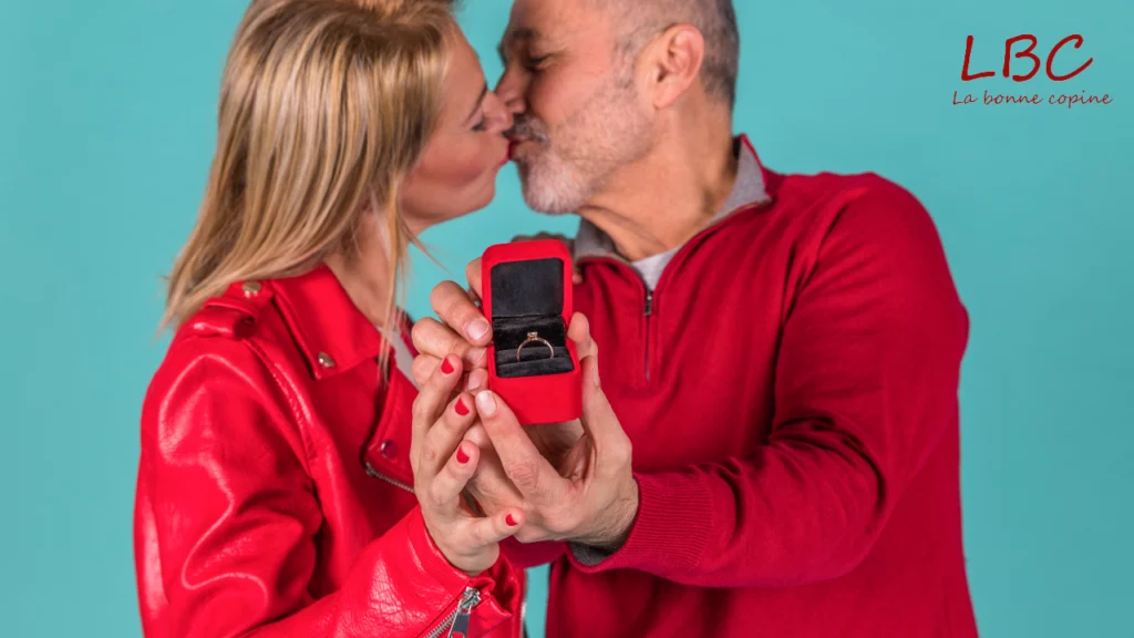 Een rood gekleed stel omhelst teder, hun handen om een verlovingsring. Een warme, intieme liefdesscène met zachte kleuren | labonnecopine.com