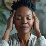 Dans un intérieur lumineux agrémenté de plantes vertes, une femme, les yeux fermés, se masse doucement les tempes. Un geste apaisant qui évoque un moment de recentrage et de bien-être naturel | labonnecopine.com