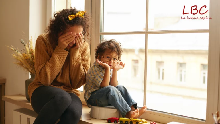 Une femme assise sur un rebord de fenêtre se couvre le visage, visiblement épuisée. À ses côtés, un petit garçon l’imite avec curiosité, entouré de jouets | labonnecopine.com