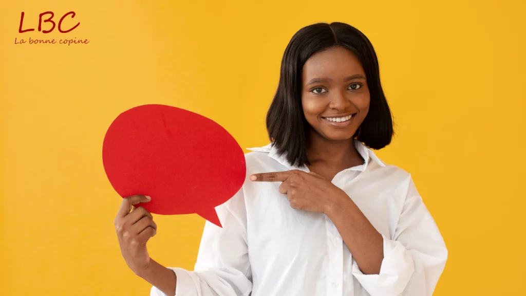 Une femme souriante tient une bulle de dialogue rouge dans une main tout en pointant du doigt avec assurance. Sur un fond jaune éclatant, sa posture dynamique et son expression enjouée attirent immédiatement l’attention, créant une scène vive et communicative
| labonnecopine.com