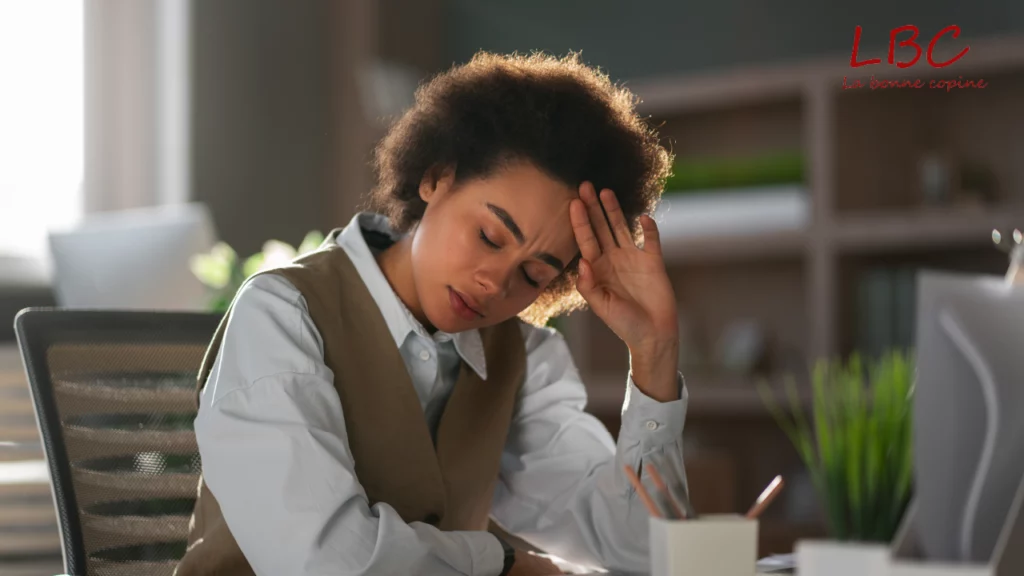Femme assise à son bureau, les yeux clos et la main sur le front, visiblement accablée par la fatigue ou le stress professionnel | labonnecopine.com