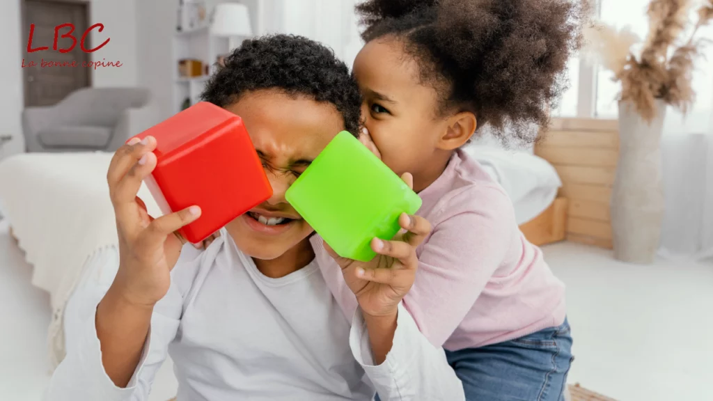 Dans un salon lumineux, deux enfants partagent un moment complice : l’un s’amuse avec des cubes colorés tandis que l’autre lui glisse quelques mots à l’oreille, entre rires et imagination | wdata-mg.info