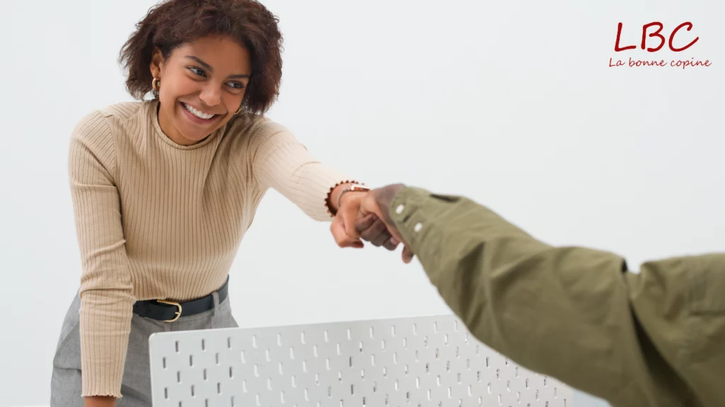 Two colleagues fist‑bump in a modern office, blending camaraderie with professional confidence.