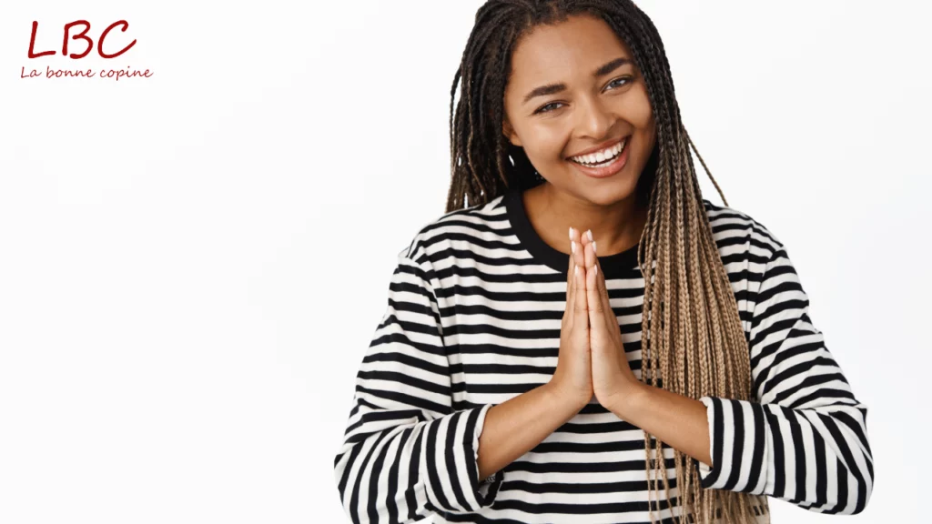 Le visage rayonnant, une jeune femme aux longues tresses et v&ecirc;tue d&rsquo;un haut ray&eacute; noir et blanc joint les mains devant elle dans un geste de gratitude sinc&egrave;re | labonnecopine.com 