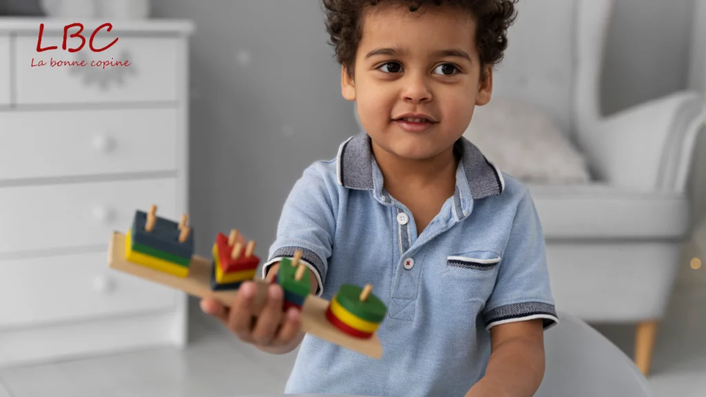 A smiling little boy proudly holding a colorful wooden toy in a modern living room | labonnecopine.com