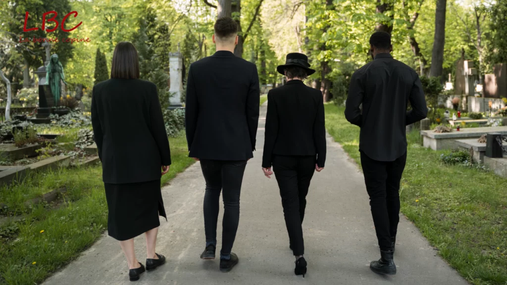 Un groupe de personnes en tenue sombre avance lentement dans un cimetière paisible, entouré de verdure, dans une atmosphère empreinte de recueillement et d’émotion | labonnecopine.com