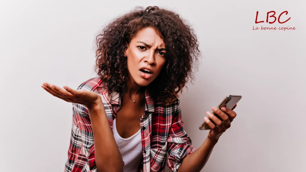 Une femme en chemise &agrave; carreaux tient son smartphone, le regard interrogateur et les sourcils l&eacute;g&egrave;rement fronc&eacute;s. Son geste d&rsquo;incompr&eacute;hension, spontan&eacute;, illustre une sc&egrave;ne famili&egrave;re : ce moment de doute face &agrave; une information d&eacute;routante | labonnecopine.com 