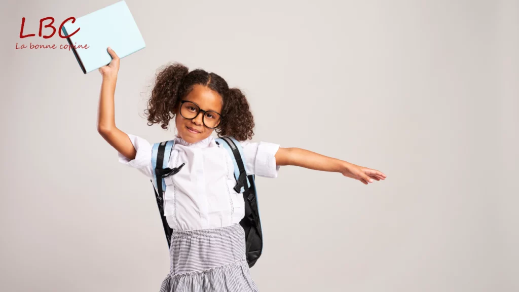 Un enfant en uniforme scolaire, sac à dos sur les épaules et carnet levé à bout de bras, exprime une joie spontanée, symbole d’enthousiasme et de motivation sur le chemin de l’apprentissage | wdata-mg.info