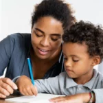 Un moment de complicité et d’apprentissage : une adulte accompagne un enfant dans sa découverte de l’écriture, symbolisant le lien précieux entre transmission et bienveillance| labonnecopine.com