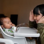 Adulte souriant interagissant avec un bébé assis dans une chaise haute | labonnecopine.com