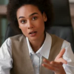 Une femme professionnelle s’exprime avec énergie dans un environnement moderne, accompagnant ses paroles de gestes engagés | labonnecopine.com