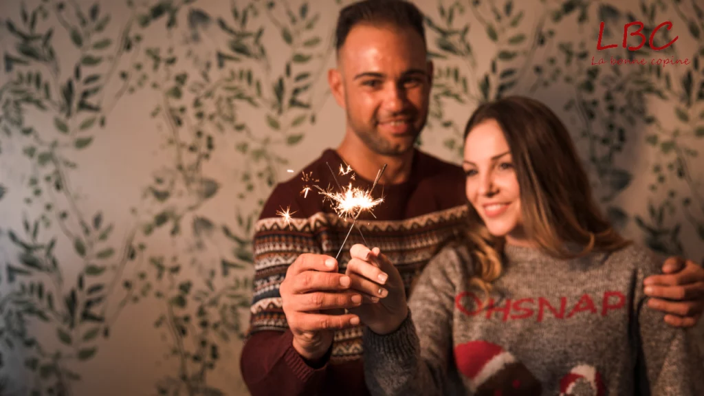 Un couple souriant tenant ensemble une étoile scintillante (sparkler), posant devant un fond végétal décoratif | labonnecopine.com