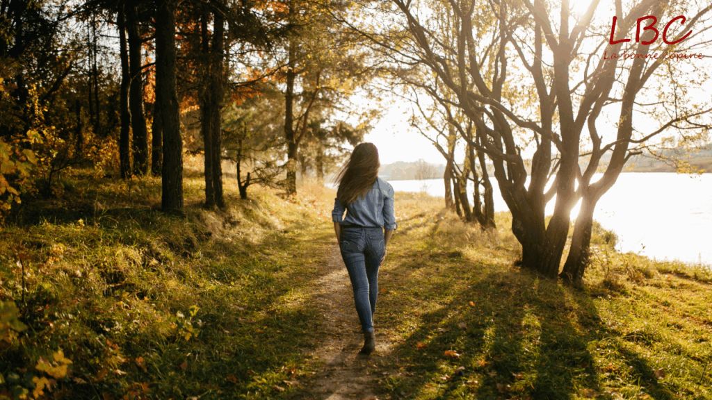 En pleine nature, une femme avance paisiblement le long d’un sentier forestier bordé par l’eau, profitant de la tranquillité du paysage. Ce moment simple incarne les bienfaits d’une promenade en milieu naturel, idéale pour se ressourcer et apaiser l’esprit | labonnecopine.com