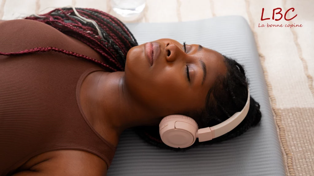 Allongée sur son tapis, les yeux paisiblement fermés, une femme s’abandonne à la quiétude d’un moment de méditation, bercée par la musique diffusée dans son casque rose | labonnecopine.com