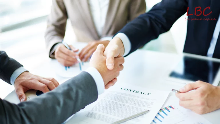 Deux personnes en costume échangent une poignée de main au-dessus d’un contrat fraîchement signé, symbolisant un accord conclu et une collaboration professionnelle scellée | labonnecopine.com