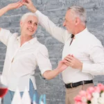 Dans une ambiance chaleureuse et festive, un couple senior partage un moment de danse complice, mêlant joie, tendresse et vitalité. Une scène qui illustre la beauté de l’amour et de la légèreté à tout âge | labonnecopine.com