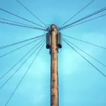 Un poteau électrique s’élève vers le ciel, ses câbles tendus dessinant des lignes qui s’étendent à l’infini. Une structure à la fois brute et graphique, symbole de connexion, d’énergie et de réseaux invisibles qui relient les lieux et les vies. | labonnecopine.com