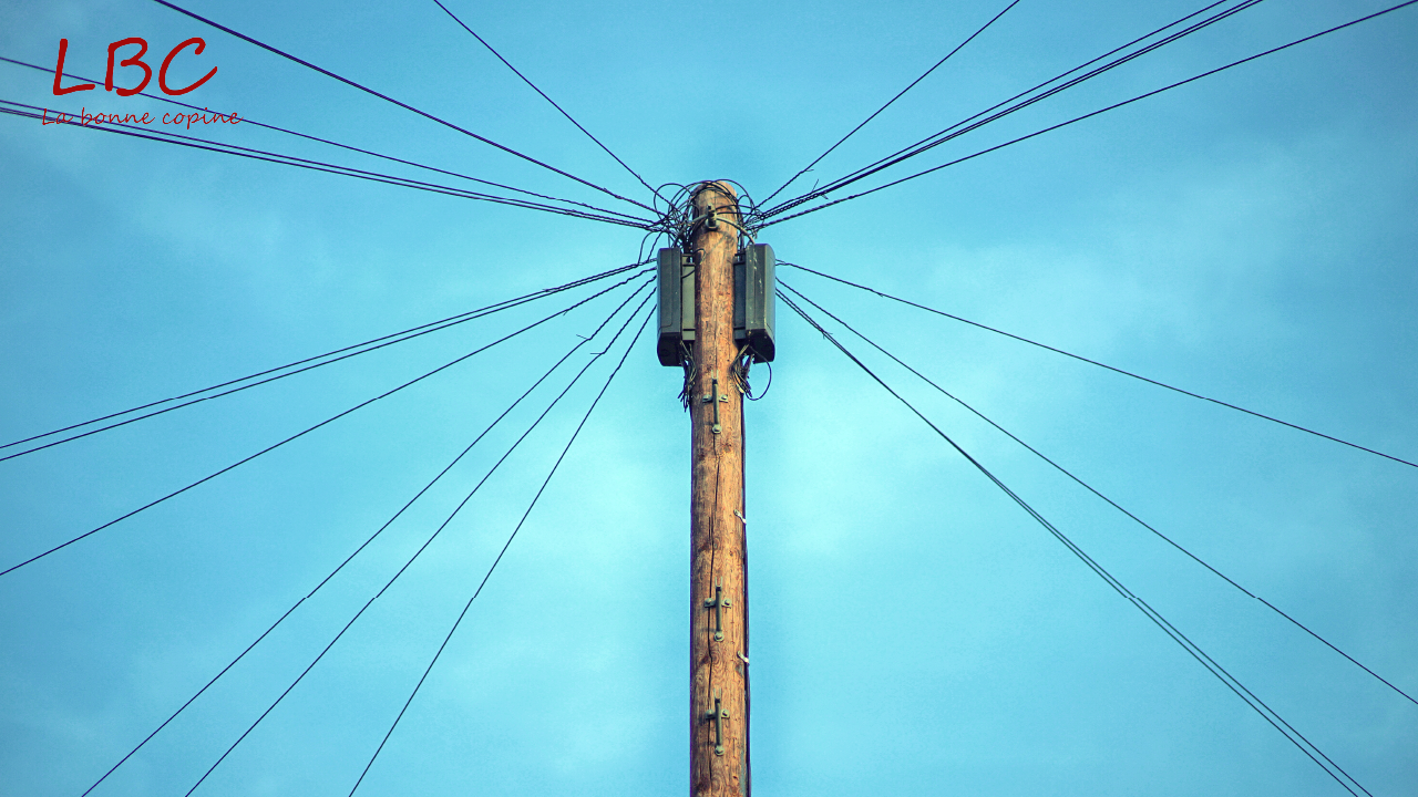 Un poteau électrique s’élève vers le ciel, ses câbles tendus dessinant des lignes qui s’étendent à l’infini. Une structure à la fois brute et graphique, symbole de connexion, d’énergie et de réseaux invisibles qui relient les lieux et les vies. | labonnecopine.com