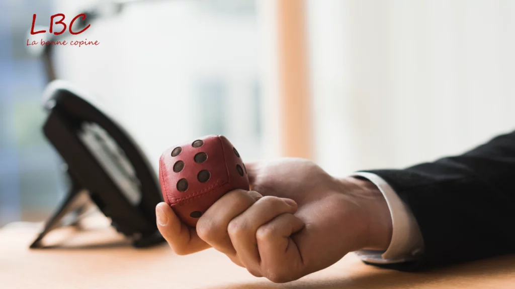 Een hand houdt zacht een rood leren dobbelsteen op een bureau, een intrigerend detail dat keuzes, spel en creativiteit oproept | labonnecopine.com