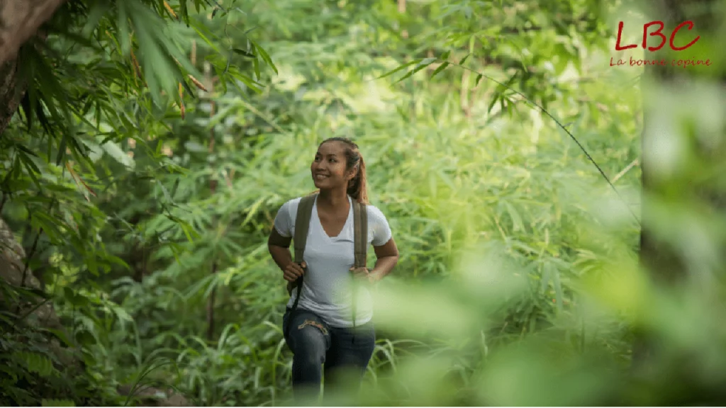 Smiling and equipped with a backpack, a woman makes her way through a lush rainforest, driven by adventure | labonnecopine.com/en