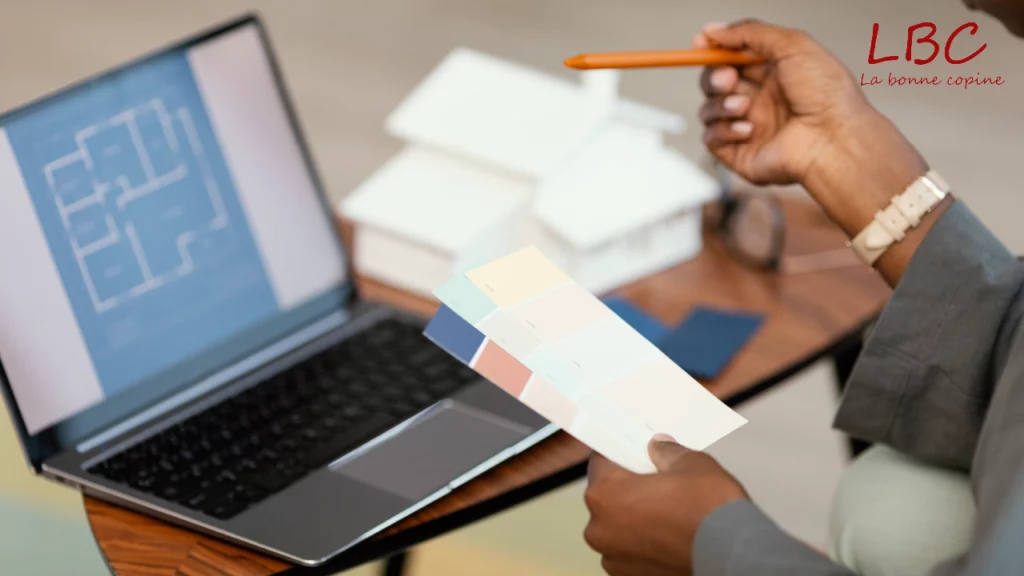 Person holding a color chart in front of a laptop displaying architectural plans | labonnecopine.com/en