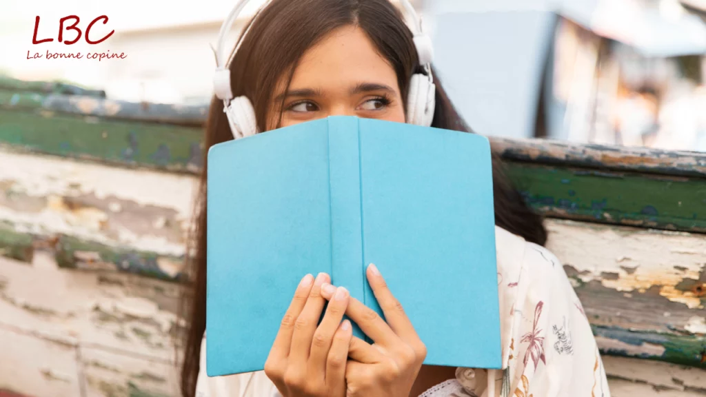 Jonge vrouw met koptelefoon, een blauw boek vasthoudend, verdiept in een auditieve en literaire wereld | labonnecopine.com