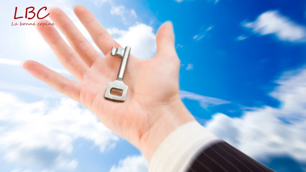 An open hand, palm open, presents a silver key catching the light, standing out brightly against a blue sky dotted with soft clouds. This image symbolizes openness, possibility and hope | labonnecopine.com