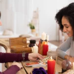 Consultation de tarot entre deux femmes autour d'une table décorée de bougies et d'objets ésotériques | labonnecopine.com