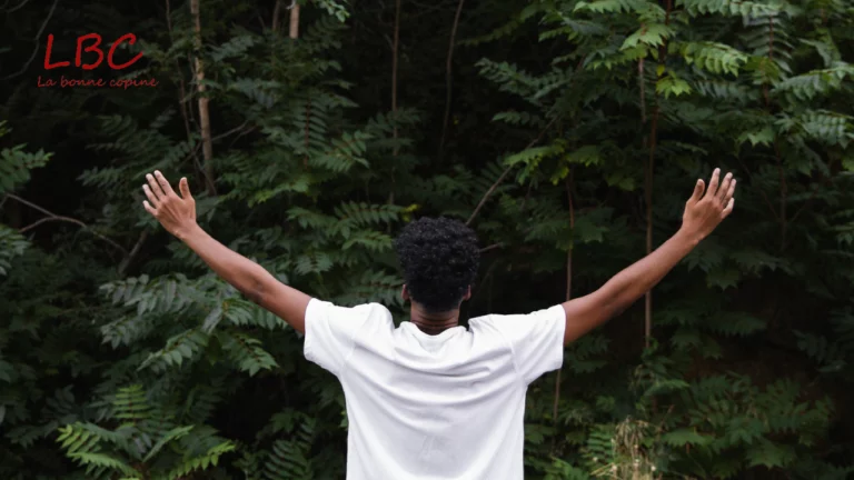 In the heart of the forest, a man in a white T-shirt raises his arms to the sky, from behind, in a gesture of openness and connection to nature | labonnecopine.com/en