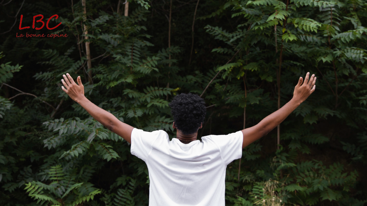 In the heart of the forest, a man in a white T-shirt raises his arms to the sky, from behind, in a gesture of openness and connection to nature | labonnecopine.com/en