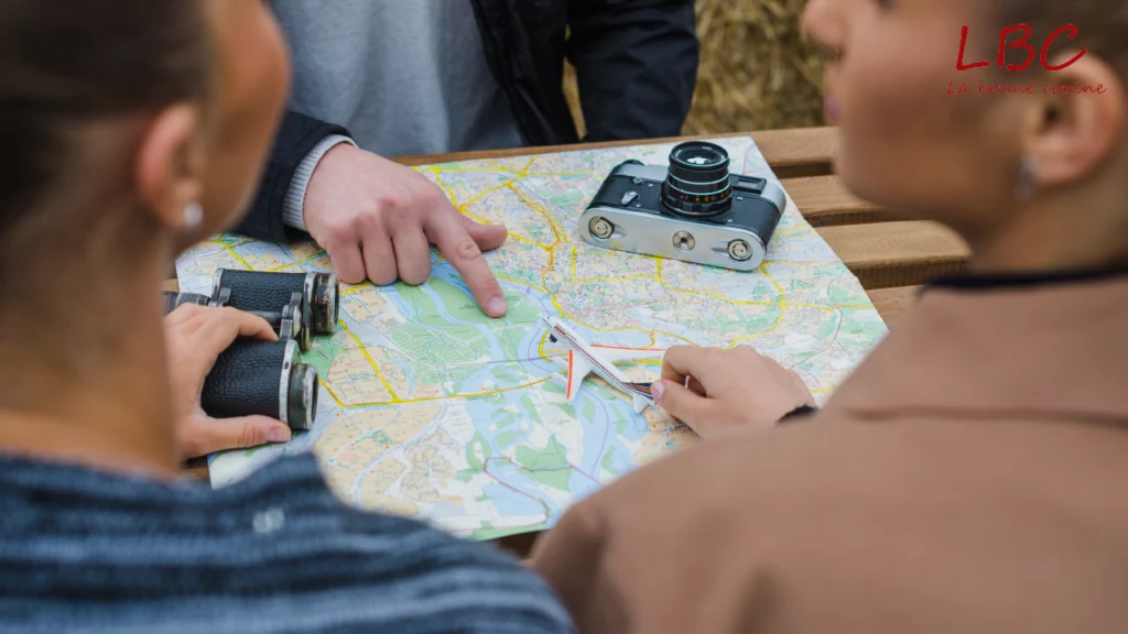 Group of people planning a route on a map with camera and binoculars on a wooden table | labonnecopine.com/en