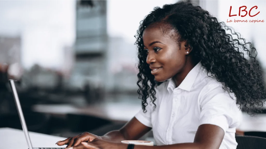 Smiling, curly-haired woman working on a laptop in a modern business environment | labonnecopine.com/en