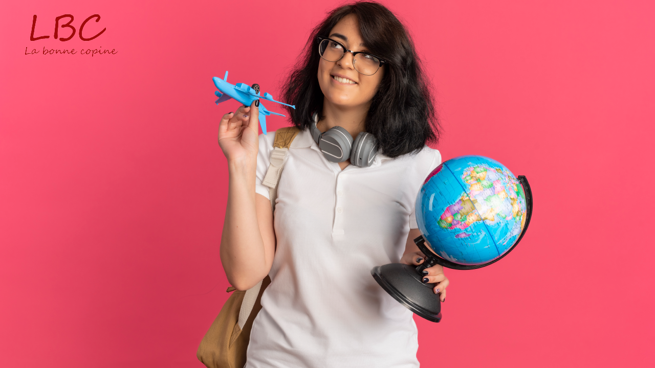 Un sourire radieux éclaire le visage d’une jeune femme qui tient avec enthousiasme un avion miniature et un globe terrestre, symboles de ses rêves d’évasion | labonnecopine.com
