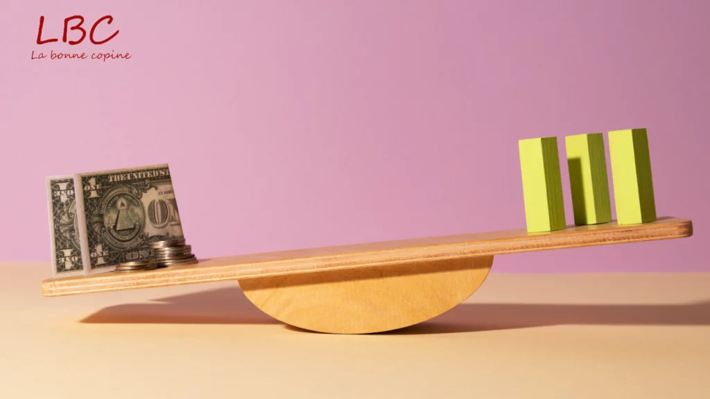 A wooden balance pits banknotes and coins on one side against minimalist yellow blocks on the other, against a soft pink background. A visual staging that questions value, balance and priorities | labonnecopine.com/en
