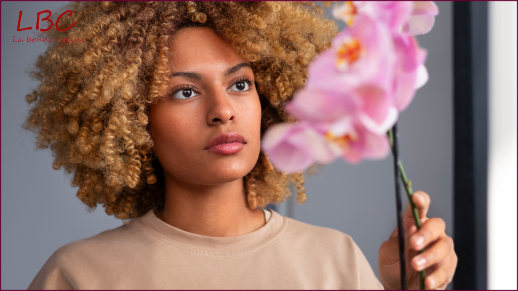 Vrouw met krullend haar houdt een roze orchidee vast en kijkt aandachtig naar de bloem