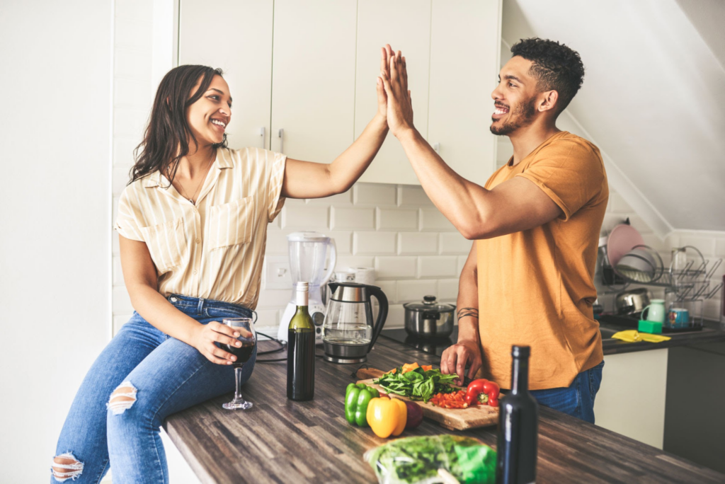 Een gelukkig stel geeft elkaar een high five in de keuken om de routine te doorbreken in hun relatie door samen te koken.