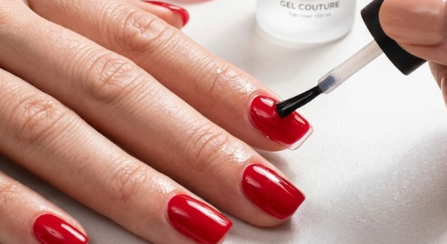 Gros plan pédagogique sur une manucure rouge brillante, montrant l'application de précision du Top Coat Gel Couture 'La Bonne Copine' et la technique de bordage de l'ongle.