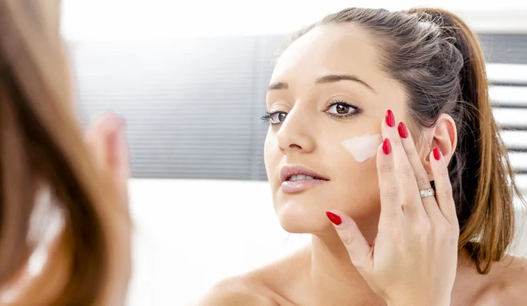 Une femme applique une petite quantité de crème sur sa joue.